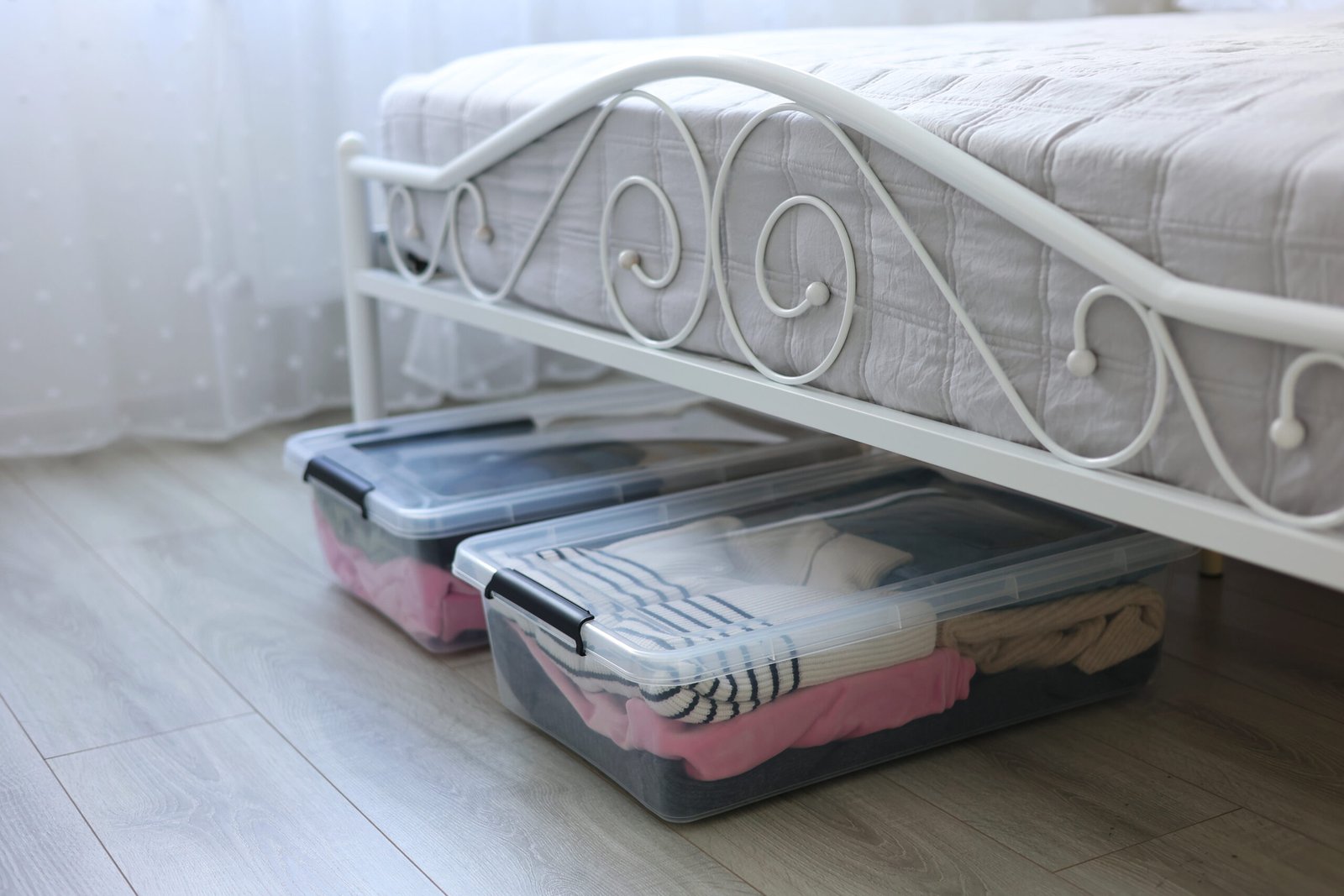 clear under-bed storage boxes with seasonal clothes neatly organised in a small bedroom