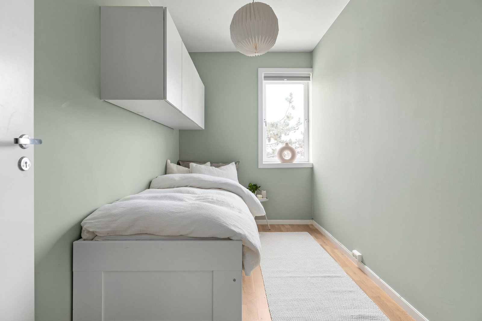 Small tidy bedroom with light walls, floating cabinets, and minimal decor.