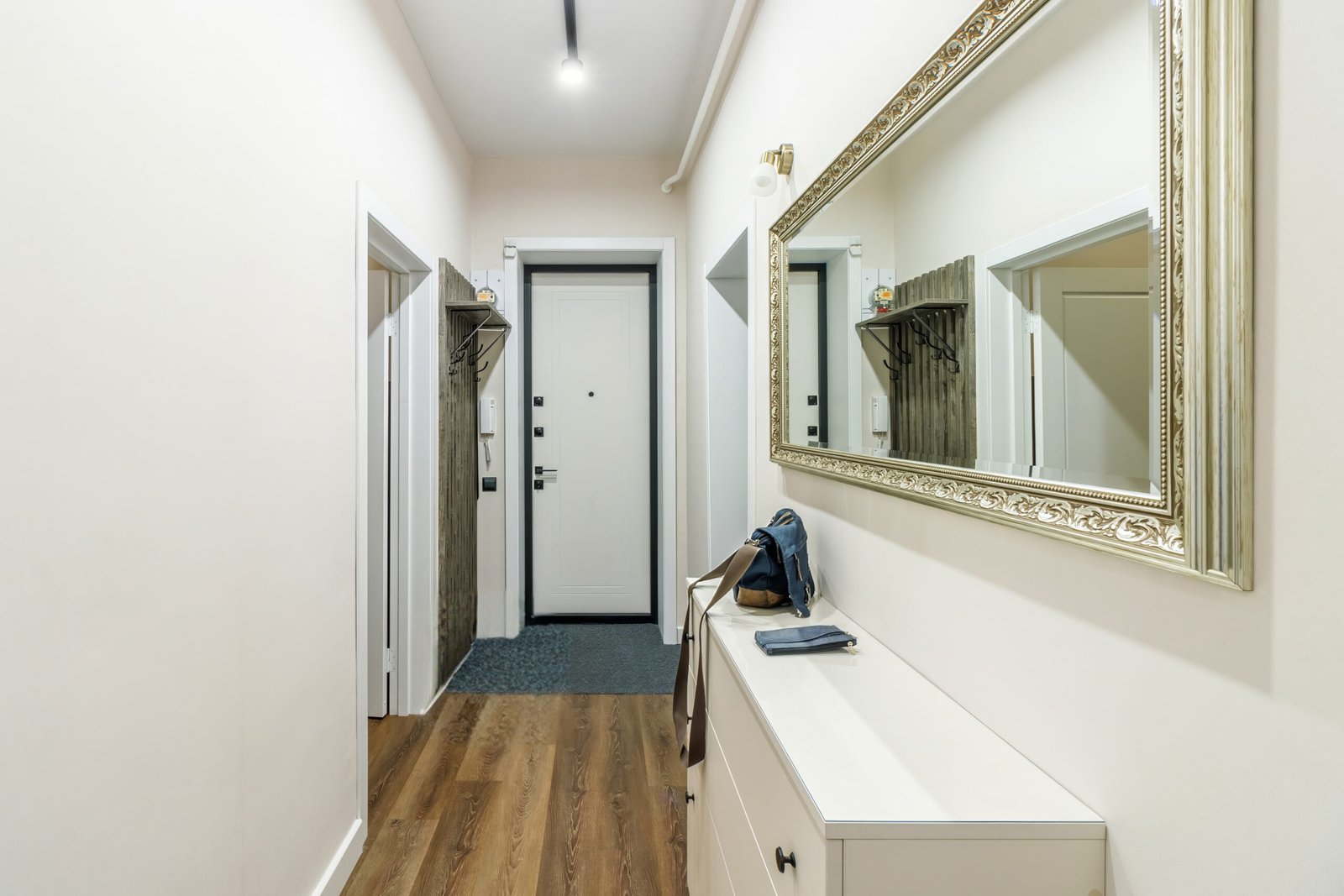 Narrow hallway with slim storage cabinet, wall-mounted hooks, and mirror that keeps the walkway clear